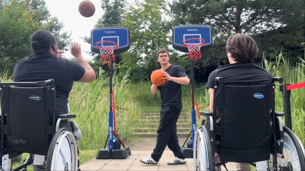 Atelier basket fauteuil en entreprise Kunto : deux collaborateurs en fauteuil roulant tirent au panier, guidés par un coach en Activité Physique Adaptée