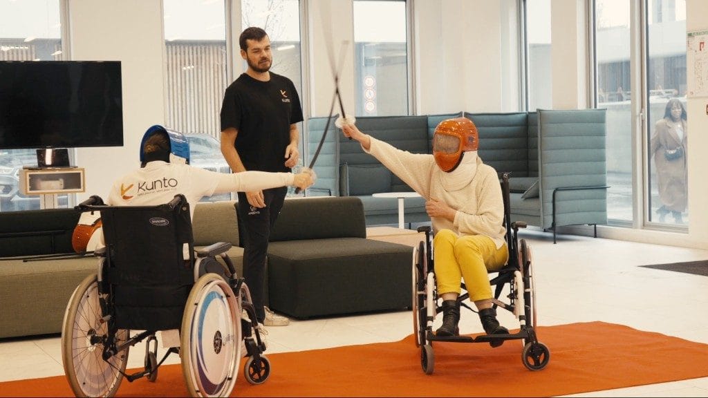 Atelier escrime handisport en entreprise Kunto : deux collaborateurs en fauteuil roulant s'affrontent à l'épée, encadrés par un coach en Activité Physique Adaptée